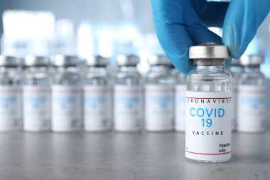 Doktor masadan COVID-19 aşısıyla cam şişe alıyor, yakın plan. Metin için boşluk
