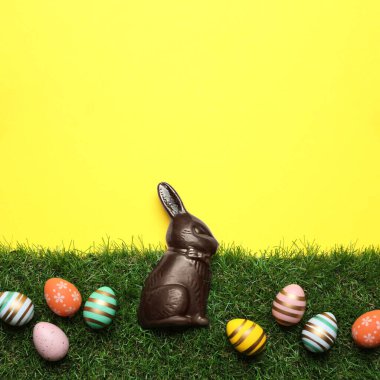 Çikolatalı Paskalya tavşanı ve sarı arka planda yeşil otlu yumurtalar.