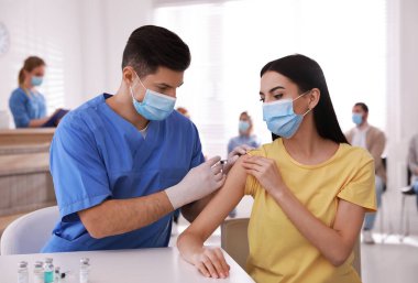 Diğerleri hastanede sırada beklerken, doktor hastaya iğne yapıyor. Aşılama kampanyası
