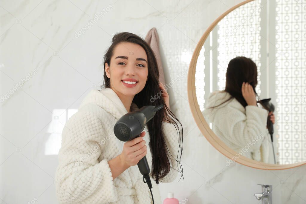 Beautiful young woman using hairdryer in bathroom