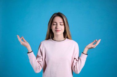 Açık mavi arka plan üzerinde meditasyon yapan genç bir kadın. Stres atma egzersizi.
