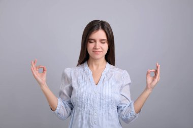 Gri arka plan üzerinde meditasyon yapan genç bir kadın. Stres atma egzersizi.
