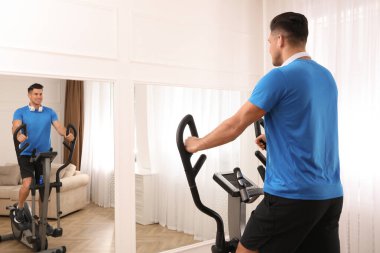 Evinde modern eliptik makine kullanan kulaklıklı bir adam.