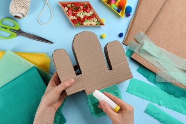 Açık mavi arka planda karton kaktüs dekore eden kadın, üst manzara. Pinata DIY
