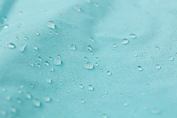Turquoise waterproof fabric with water drops as background, closeup