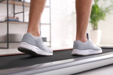 Adam evde yürüyüş bandında antrenman yapıyor, yakın plan.