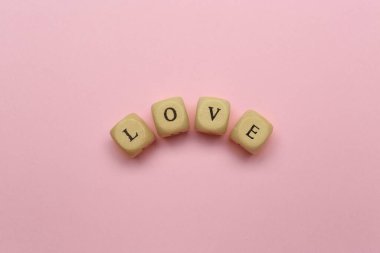 İçinde harfler olan mini küpler pembe arka planda aşk sözcükleri oluşturur.