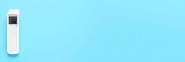 Açık mavi arkaplanda kızılötesi termometre, metin için boşluk olan üst görünüm. Covid-19 salgını sırasında sıcaklık kontrol ediliyor