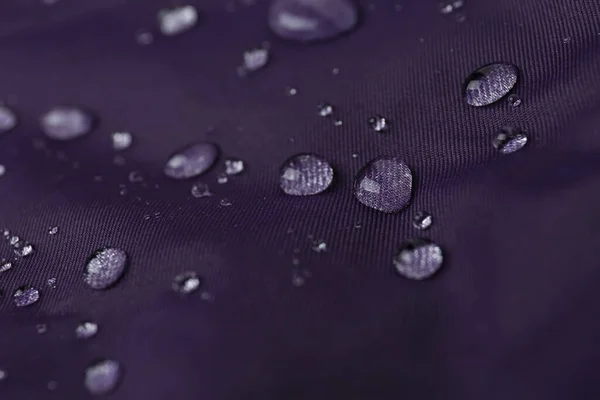 Purple waterproof fabric with water drops as background, closeup