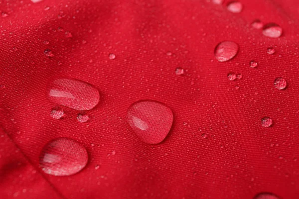 Red waterproof fabric with water drops as background, closeup
