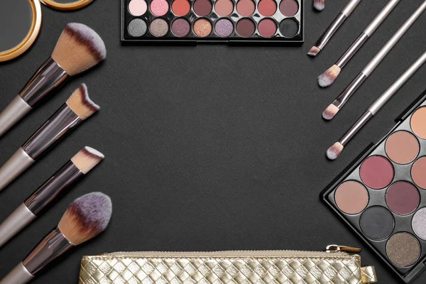 Flat lay composition with professional makeup brushes and eye shadow palettes on black background, space for text