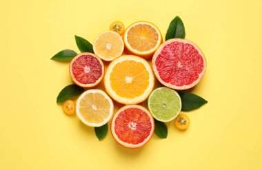 Açık sarı arka planda yeşil yapraklı taze sulu narenciye meyveleri.