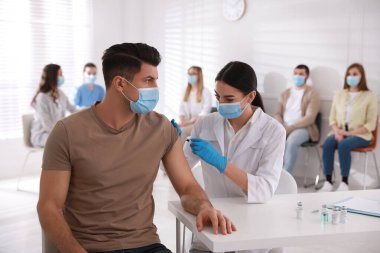 Diğerleri hastanede sırada beklerken, doktor hastaya iğne yapıyor. Aşılama kampanyası