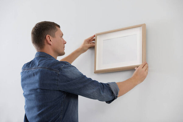 Мужчина вешает картину на белую стену в помещении. Интерьер