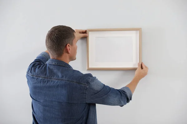 Man hanging picture on white wall indoors. Interior decoration