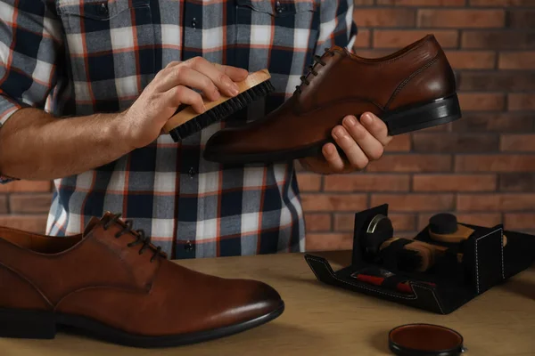 Man taking professional care of brown leather shoes in workshop, closeup