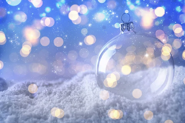 Transparent Christmas ball on snow against blurred fairy lights, space for text. Bokeh effect