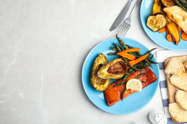 Lezzetli pişmiş somon ve sebzeler gri masada servis ediliyor, düzlük ve yazı için yer var. Kızartmadan sağlıklı yemekler.