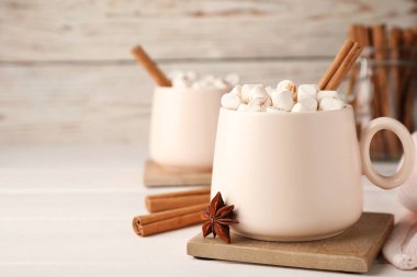 Bir fincan kremalı sıcak içecek ve beyaz masada aromatik tarçın. Metin için boşluk