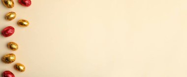 Bej arka planda kırmızı ve altın folyoya sarılı çikolatalı yumurtalar. Metin için boşluk