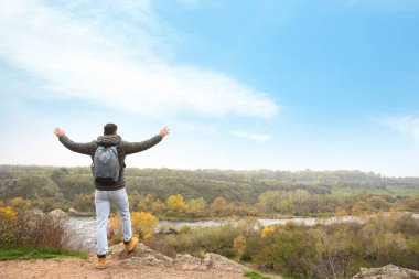 Sırt çantalı bir gezgin, dağ nehri kenarında, arka manzaralı.