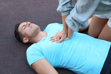 Genç bir kadın dışarıda baygın bir adama kalp masajı yapıyor. İlk yardım