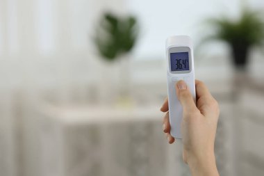 Kızıl ötesi termometresi olan kadının yakın görüntüsü bulanık arka planda, mesaj için yer var. Covid-19 salgını sırasında sıcaklık kontrol ediliyor