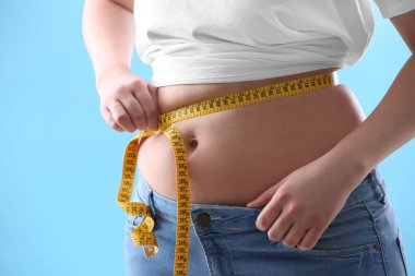 Açık mavi arka planda mezurası olan kadın, yakın plan. Yeni yıl partisinden sonra aşırı kilo sorunu