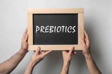 Hafif arkaplanda PreBIOTICS sözcüğünün yazılı olduğu tahtayı tutan adamlar, yakın plan 