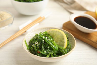 Beyaz ahşap masada servis edilen limon dilimli Japon yosun salatası.