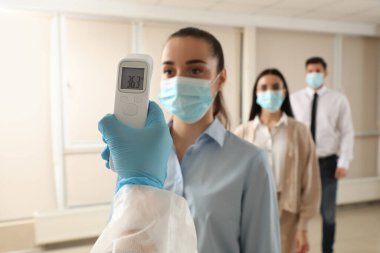 Ofisteki çalışanların sıcaklığını ölçen doktor, yakın çekim. Covid-19 'un yayılmasını engelle
