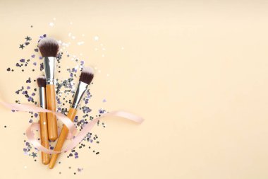 Farklı makyaj fırçaları, kurdele ve bej arka planda parlak konfeti. Metin için boşluk