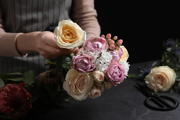 Florist making beautiful bouquet at black table, closeup