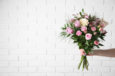 Beyaz tuğla duvarın yanında gül buketi olan bir kadın, yakın plan. Metin için boşluk