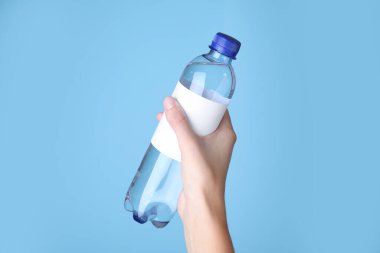 Açık mavi arka planda elinde soda olan plastik şişe tutan kadın, yakın plan.