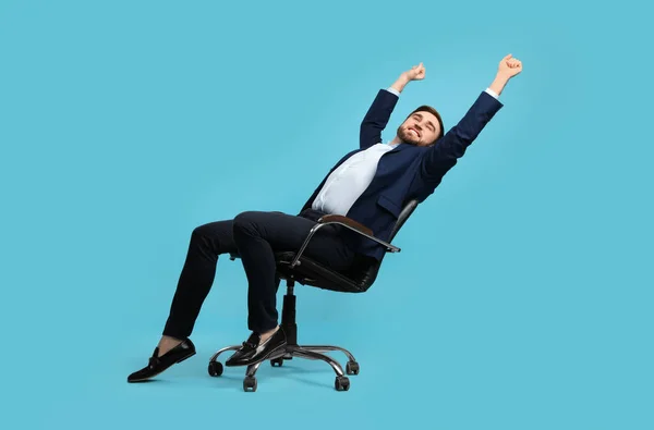 Young businessman stretching in comfortable office chair on turquoise background
