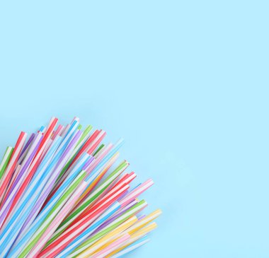 Açık mavi arka planda renkli plastik pipet yığınları, düz yatış. Metin için boşluk