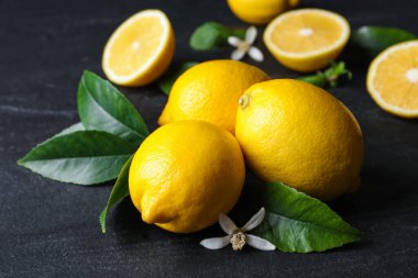 Yeşil yapraklı taze limonlar ve siyah masadaki çiçekler, yakın plan.