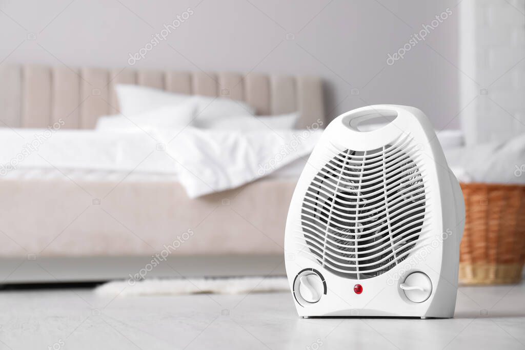 Modern electric fan heater on floor in light bedroom. Space for text