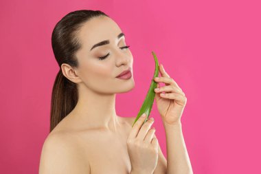 Pembe arka planda aloe vera yaprağı olan genç bir kadın.