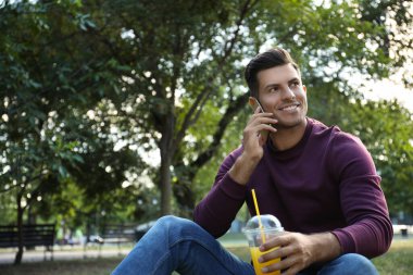Serinletici içkisi olan yakışıklı adam parkta akıllı telefondan konuşuyor.