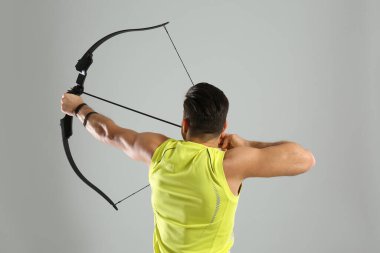 Ok ve yay kullanan bir adam açık gri arka planda okçuluk yapıyor.