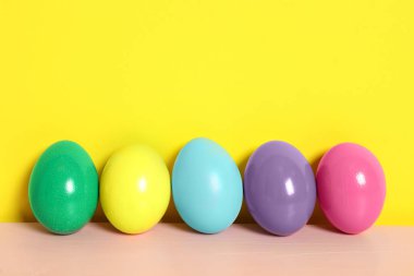 Pembe ahşap masadaki Paskalya yumurtaları sarı arka plana karşı, metin için boşluk
