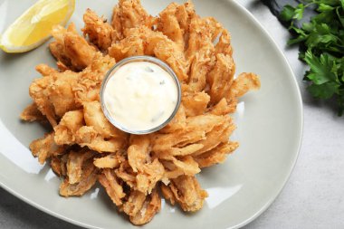 Kızarmış soğan ve sos. Gri masada servis ediliyor.