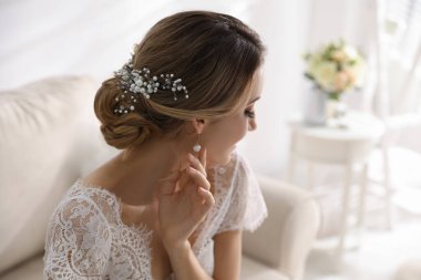 Genç gelin, zarif düğün saç stiliyle odada.