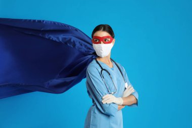 Açık mavi arka planda süper kahraman gibi giyinmiş bir doktor. COVID-19 ile savaşan tıp çalışanları kavramı
