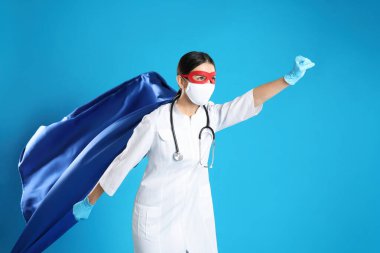 Açık mavi arka planda süper kahraman gibi giyinmiş bir doktor. COVID-19 ile savaşan tıp çalışanları kavramı