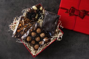 Çikolatalı ve şekerli hediye kutusu koyu gri masada, üst tarafta.