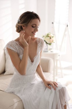 Gorgeous bride in beautiful wedding dress on sofa in room