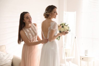 Gelinin gelinliğini giymesine yardım eden genç bir kadın.